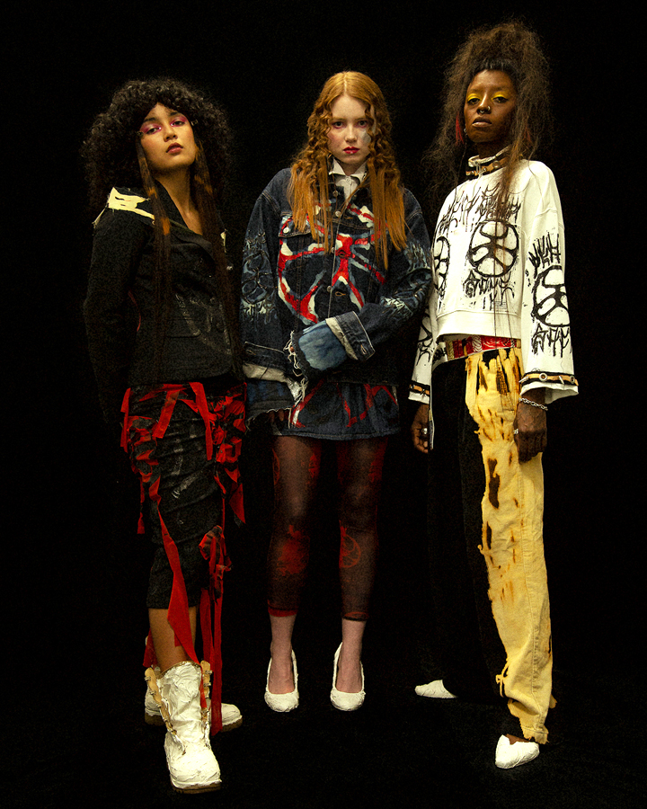 Three models in distressed clothing on a black backdrop looking at the camera